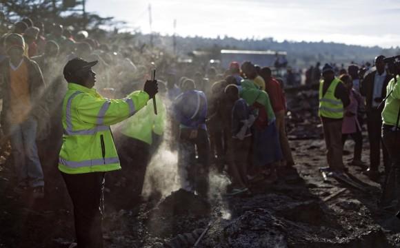 A member of the emergency services takes a photo using his tablet, as onlookers gather at the still-smouldering scene of an accident involving a tanker near Naivasha, in Kenya, on Dec. 11, 2016. (AP Photo/Ben Curtis)