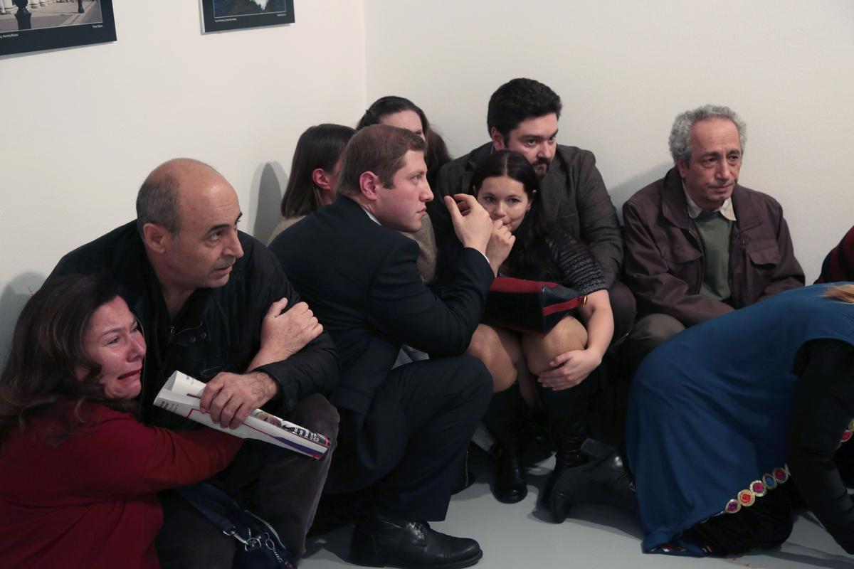 People crouch in a corner after Andrei Karlov, the Russian Ambassador to Turkey, was shot at a photo gallery in Ankara, Turkey, on Dec. 19, 2016. (AP Photo/Burhan Ozbilici)