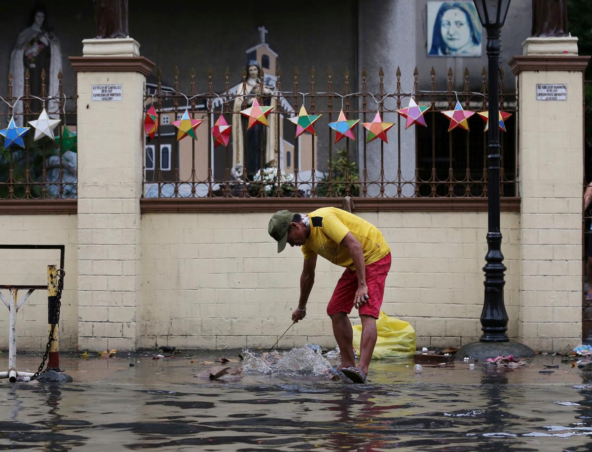A man cleans the trash along a flooded area outside a church caused by rains from Typhoon Nock-Ten in Quezon city, north of Manila, Philippines on on Dec. 26, 2016. (AP Photo/Aaron Favila)