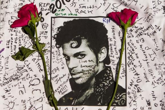 In this April 22, 2016 file photo, flowers lie on a T-shirt signed by fans at a makeshift memorial for musician Prince outside the Apollo Theater in New York. The singer died April 21, 2016, at the age of 57. With the loss of several icons of Generation X's youth, the year 2016 has left the generation born between the early 1960s and the early 1980s, wallowing in memories and contemplating its own mortality. (AP Photo/Andres Kudacki, File)