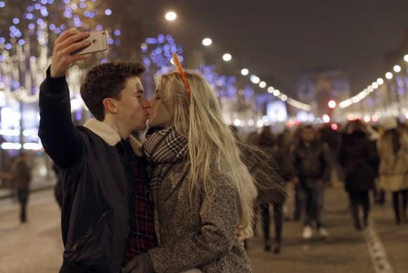 A man takes a picture as he kisses his companion during the New Year's Eve celebration on the Champs Elysees, in Paris, France, on Jan.1, 2017. (AP Photo/Christophe Ena)
