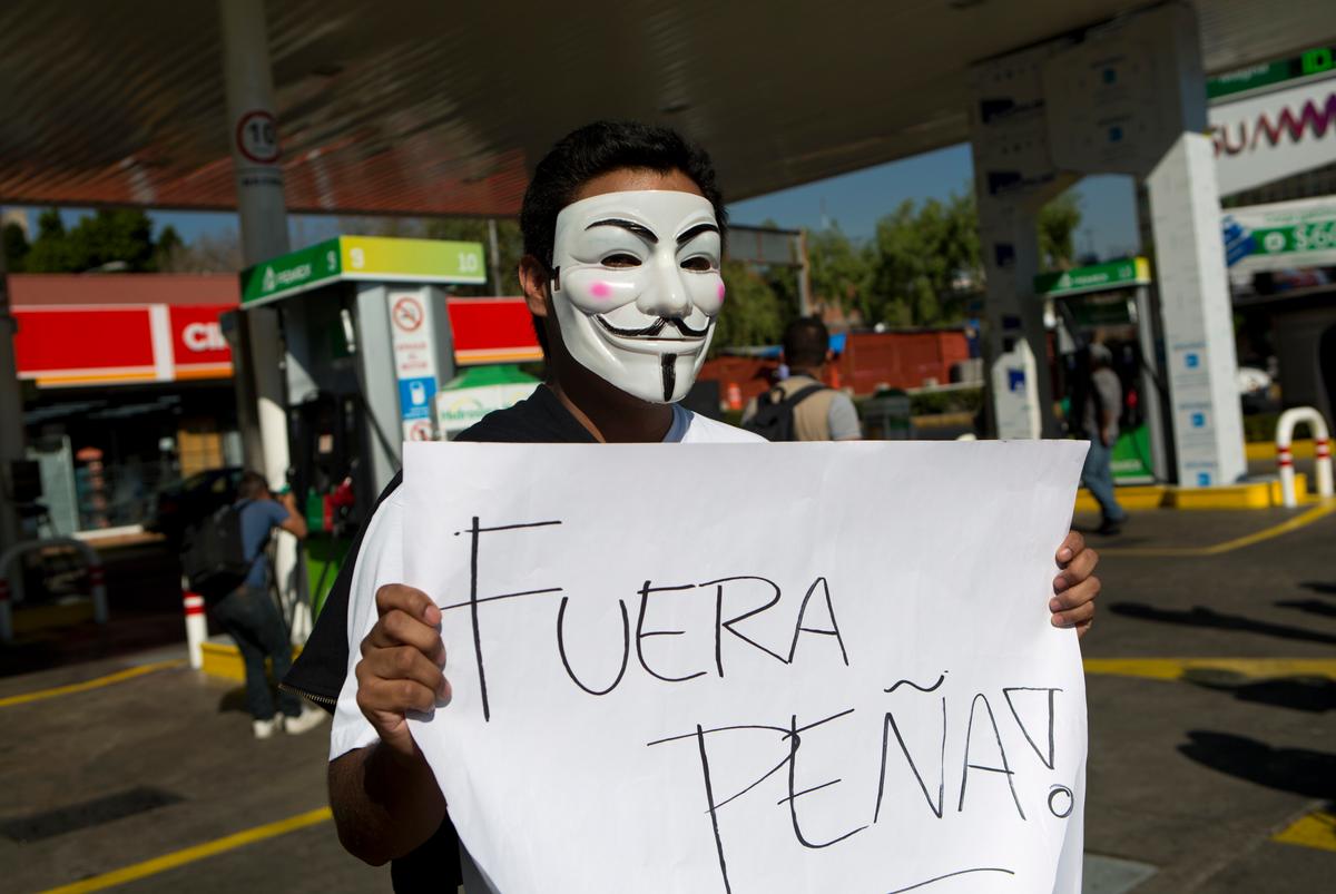 A protester with a Guy Fawkes masks holds a sign that says in Spanish "Pena Out!" as people angry over hiked gas prices under President Enrique Pena Nieto's government block for hours one of the city's oldest gas stations at main intersection in Mexico City on Jan. 2, 2017. (AP Photo/Rebecca Blackwell)