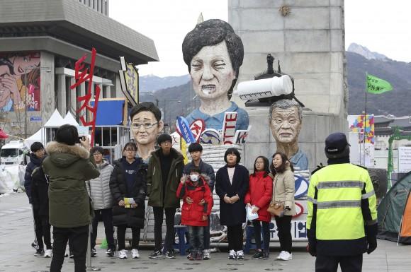 People pose for photos in front of effigies of impeached South Korean President Park Geun-hye, center, Hyundai Motor Co. Chairman Chung Mong-koo and Samsung Electronics Co. Vice Chairman Lee Jae-yong, left, in Seoul, South Korea, on Jan. 5, 2017. (AP Photo/Ahn Young-joon)