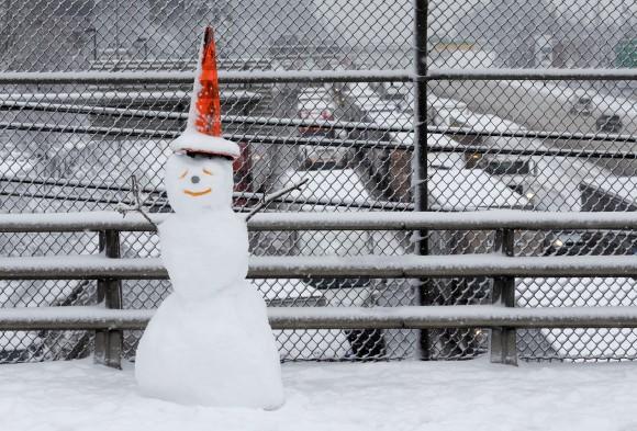 A snowman wearing a traffic cone hat is shown on an overpass as early morning traffic is at a standstill in the background on Interstate 5 headed into Portland, Ore., on Jan. 11, 2017. (AP Photo/Don Ryan)