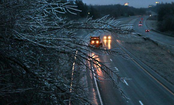 A Missouri Department of Transportation salt truck spreads ice melt on Interstate 55 as coated tree branches sway overhead as seen from the Main Street bridge in Festus, Mo., on Jan. 13, 2017. (Robert Cohen/St. Louis Post-Dispatch via AP)