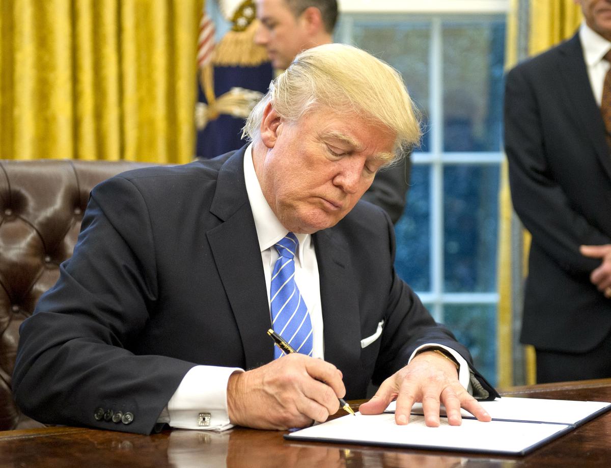 President Donald Trump signs the last of three Executive Orders in the Oval Office of the White House in Washington, DC, on Jan. 23, 2017. (Ron Sachs - Pool/Getty Images)
