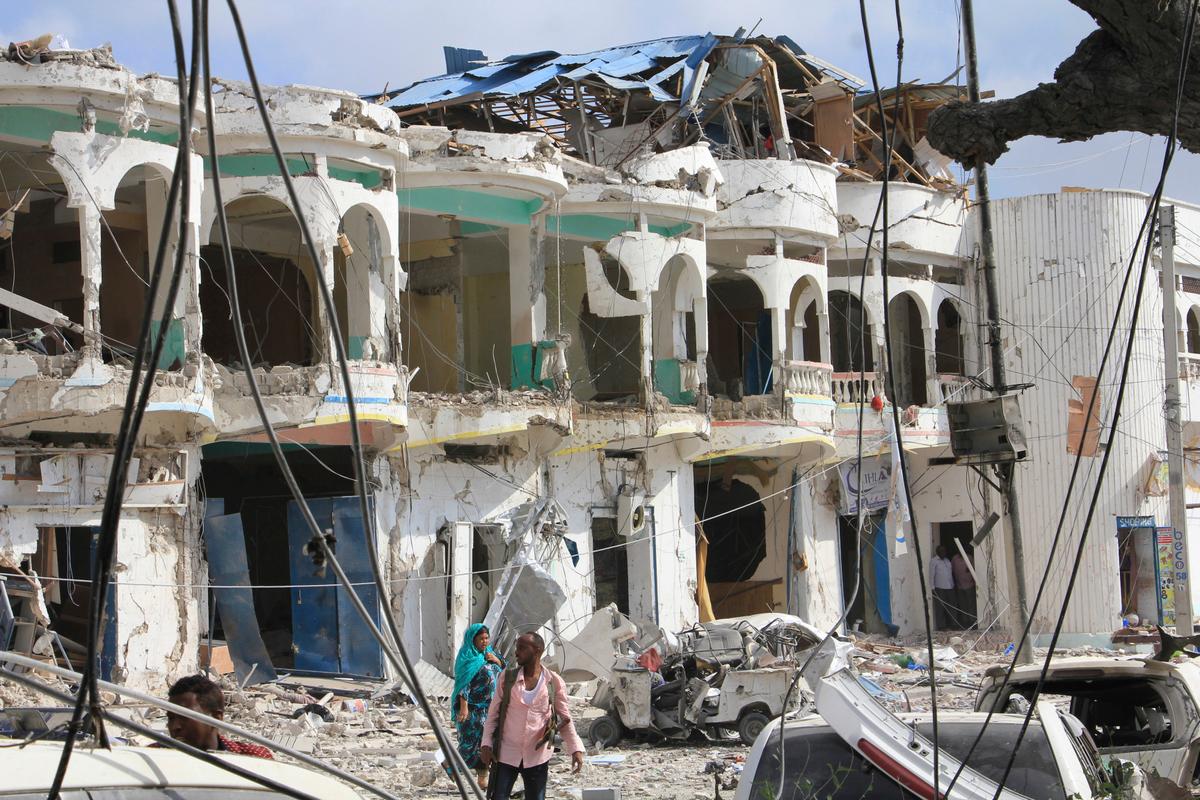 Somalis walk near a hotel heavily damaged by a car bomb blast in Mogadishu, Somalia on Jan 25, 2017. (AP Photo/Farah Abdi Warsameh)