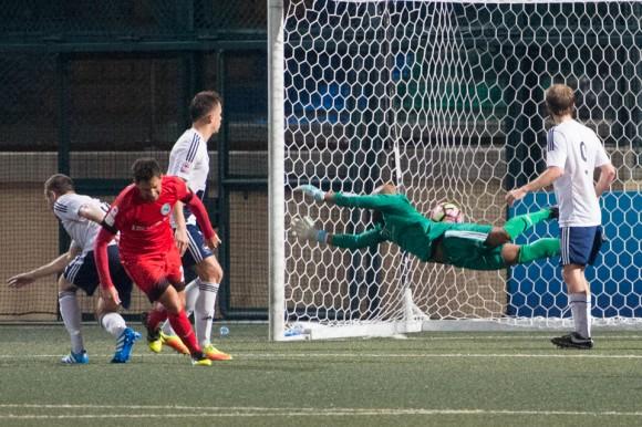 Roberto Fronza scores KC Southern's 5th goal under HKFC keeper, Issey Maholo's body as he dives to his right. (Bill Cox/Epoch Times)