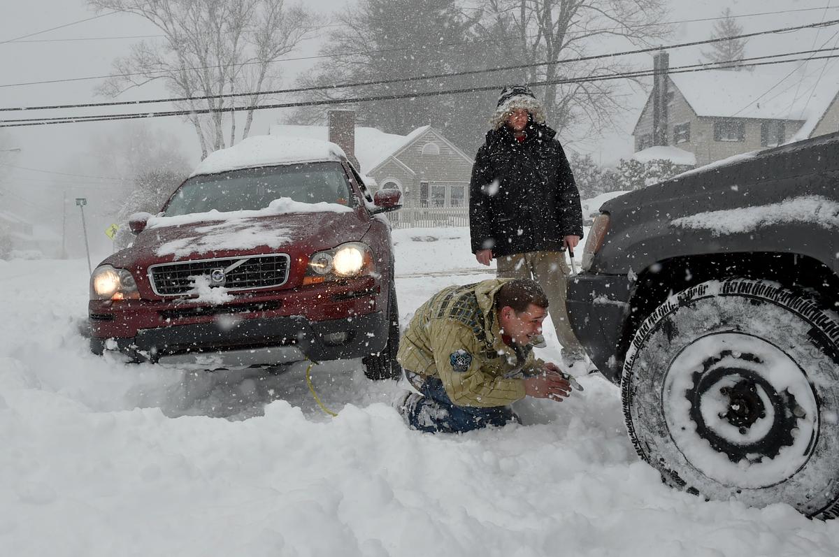 Nick Sinon looks for a place to attach his tow-strap to the front of his four wheel drive Jeep as he and Brian Brady try to help a stranded motorist get out of a snowbank in Bristol, Conn., on Feb. 9, 2017. (John Woike/Hartford Courant via AP)