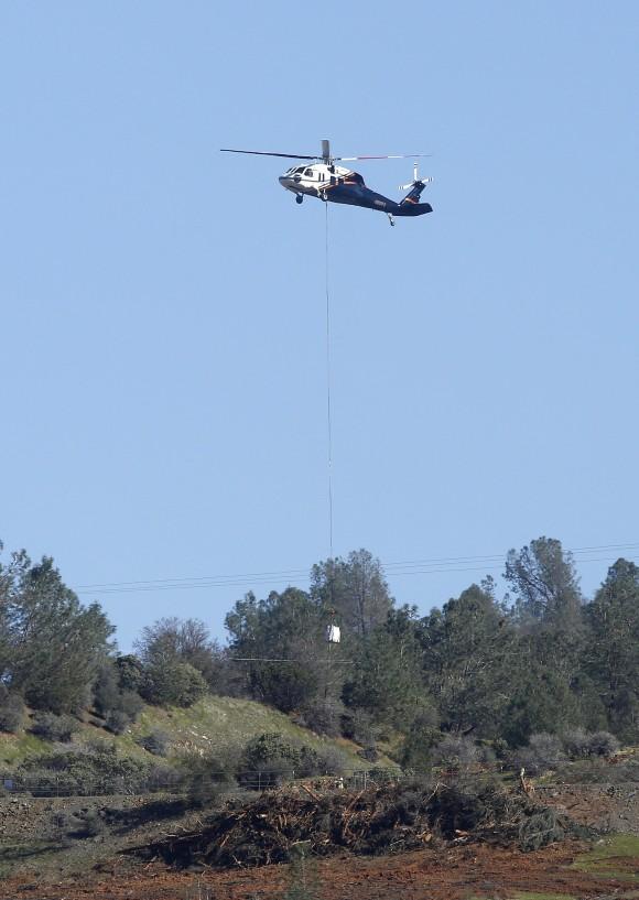 A helicopter lowers a load of rocks to fill in a hole near the Oroville Dam's emergency spillway, Tuesday, Feb. 14, 2017, in Oroville, California. (AP Photo/Rich Pedroncelli)