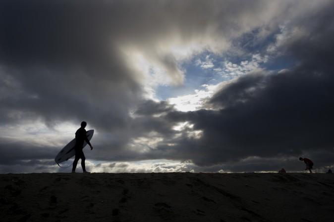 Surfer Bradley Domke walks along a sand berm as storm clouds gather overhead in Seal Beach, Calif., Feb. 18. (AP Photo/Jae C. Hong)