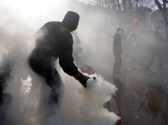 An activist throws a smoke grenade toward riot police during a protest rally in front of the President Office in Kiev, Ukraine on Feb. 19, 2017. Protesters were demanding a stop to trade relations with Russia-occupied Ukrainian territories. (AP Photo/Efrem Lukatsky)
