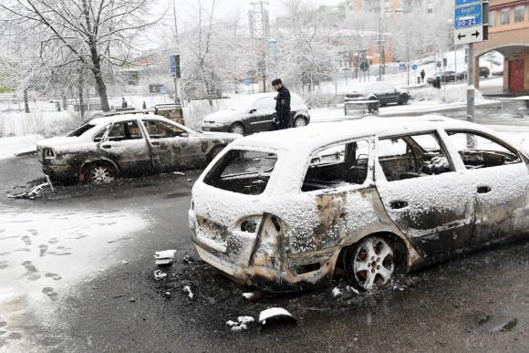 A policeman investigates a burned out car in the suburb of Rinkeby outside Stockholm on Feb. 20, 2017. Police in Sweden said Tuesday they were investigating riots that broke out overnight in a predominantly immigrant Stockholm suburb after officers arrested a suspect on drug charges. Spokesman Lars Bystrom said unidentified people, including some wearing masks, threw rocks at police, set cars on fire and looted shops in Rinkeby, north of Stockholm. (Christine Olsson/TT News Agency via AP)