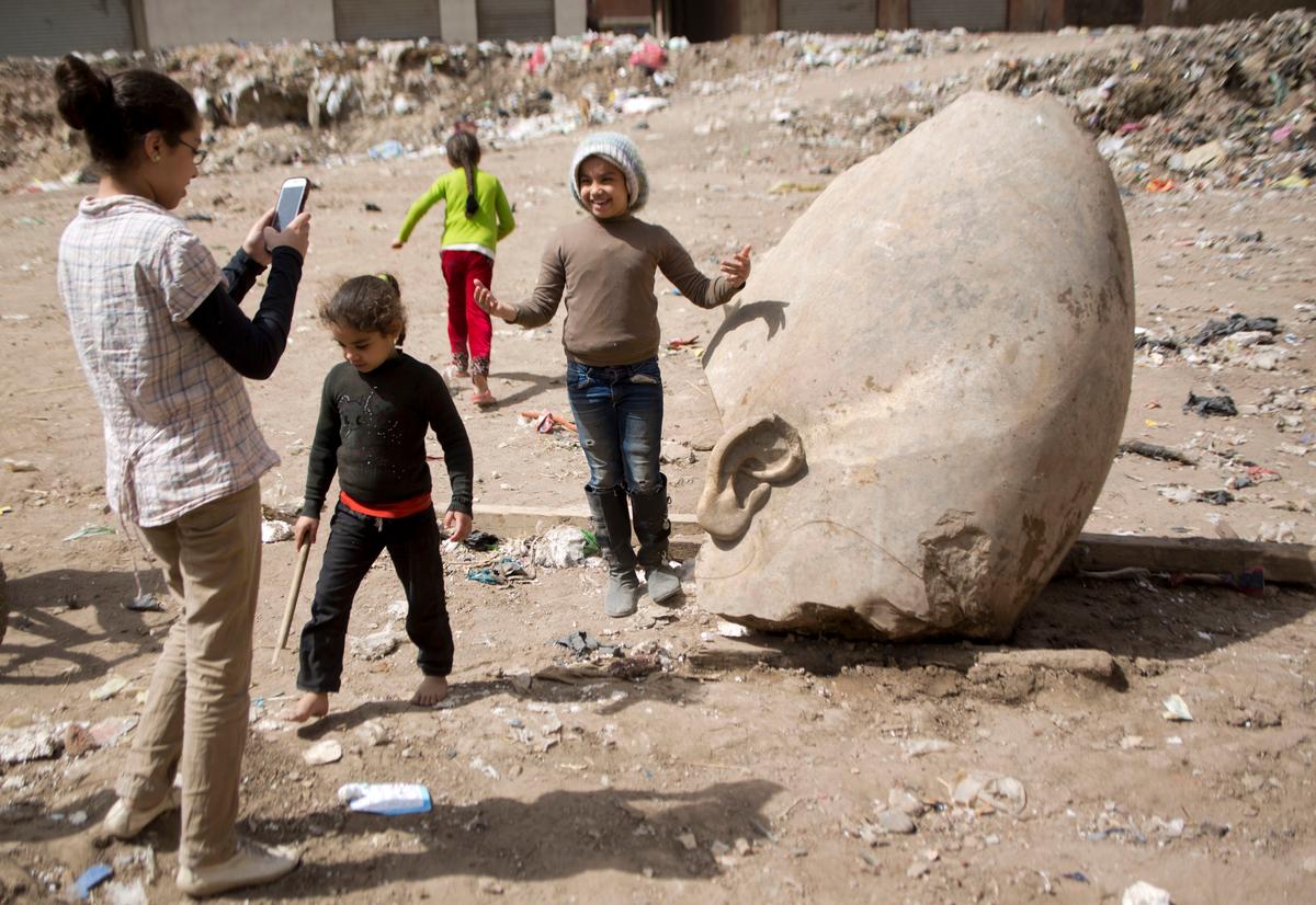A child poses for a picture past a recently discovered statue in a Cairo slum that may be of pharaoh Ramses II, in Cairo, Egypt on March 10, 2017. (AP Photo/Amr Nabil)