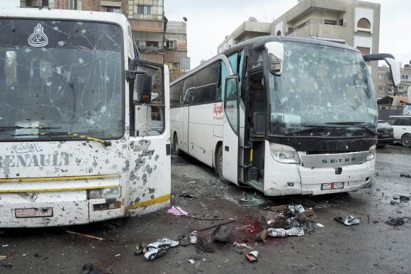 Blood soaked streets and several damaged buses in a parking lot at the site of an attack by twin explosions in Damascus, Syria on March 11, 2017. (SANA via AP)