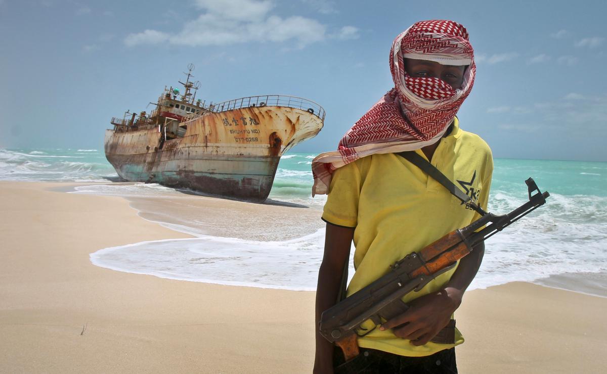 Masked and armed Somali pirate Hassan stands near a Taiwanese fishing vessel washed ashore after the pirates were paid a ransom and the crew were released in the once-bustling pirate den of Hobyo, Somalia on Sept. 23, 2012. (AP Photo/Farah Abdi Warsameh)
