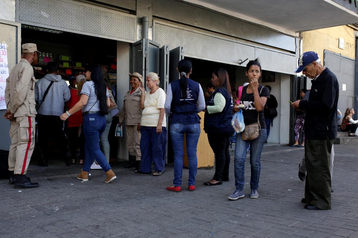 Militia officers stand guard at the entrance of a bakery as people line up to buy bread in Caracas, Venezuela on March 17, 2017. (REUTERS/Marco Bello)