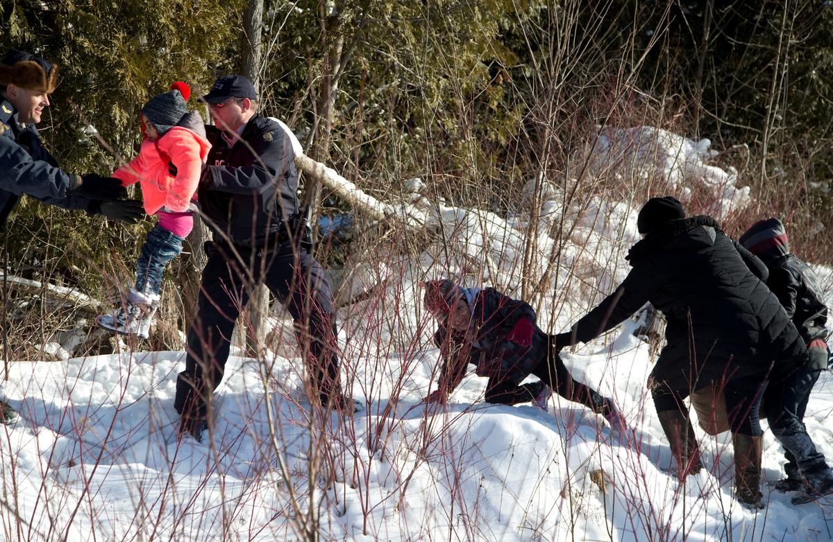 Royal Canadian Mounted Police (RCMP) officers assist a child from a family that claimed to be from Sudan as they walk across the U.S.-Canada border into Hemmingford, Canada, from Champlain in New York, U.S. on Feb. 17, 2017. (REUTERS/Christinne Muschi)