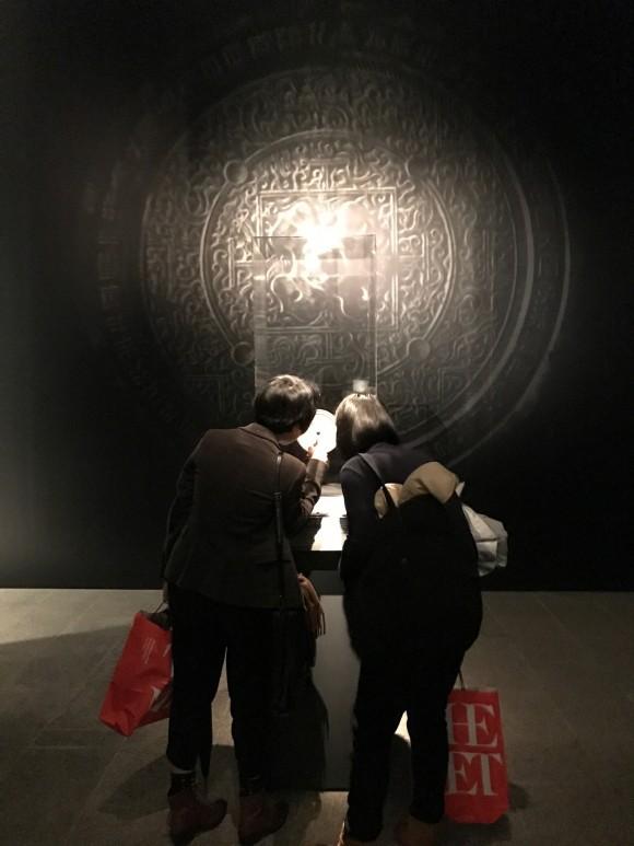 Two women look at the Han Dynasty mirror on display at the Age of Empires exhibition at The Metropolitan Museum of Art. (Milene Fernandez/Epoch Times)