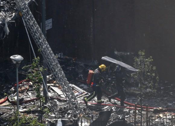 A police officer holds a riot shield over a firefighter at a tower block severely damaged by a fire in West London, Britain on June 14, 2017. (REUTERS/Neil Hall)