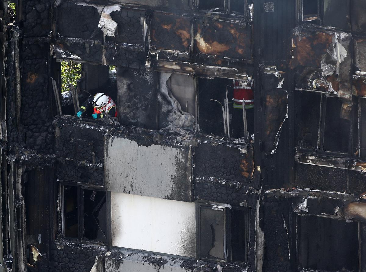 A firefighter examines material in a tower block severely damaged by fire in West London, Britain on June 14, 2017. (REUTERS/Neil Hall)
