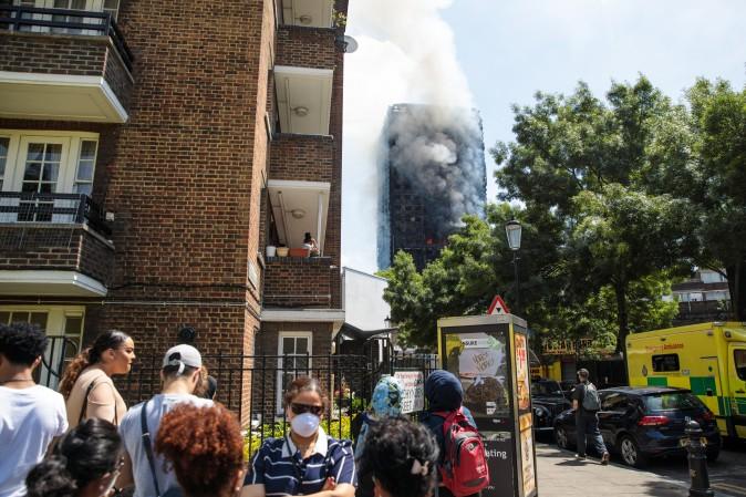 People look on as smoke rises from the burning building after a huge fire engulfed the 24 storey residential Grenfell Tower block in Latimer Road, West London in the early hours of this morning on June 14, 2017 in London, England. The Mayor of London, Sadiq Khan, has declared the fire a major incident as more than 200 firefighters are still tackling the blaze while at least six are dead and 20 are in critical care. (Photo by Jack Taylor/Getty Images)