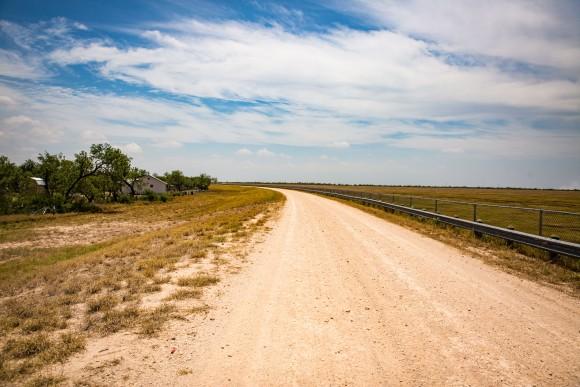 The levee road behind the tiny border town of Granjeno, Texas, on May 28. The levee, which doubles as a border barrier, drops about 18 feet to the right, and Granjeno is seen to the left. The Rio Grande is almost a mile south of the levee. (Benjamin Chasteen/The Epoch Times)
