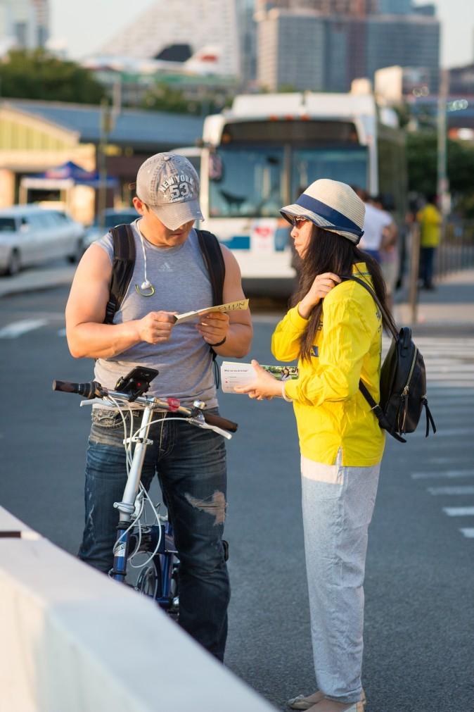 A Falun Gong practitioner hands out pamphlets about the practice and the Chinese regime's persecution campaign to a passerby near the Chinese Consulate in New York on July 16, 2017. (Benjamin Chasteen/The Epoch Times)
