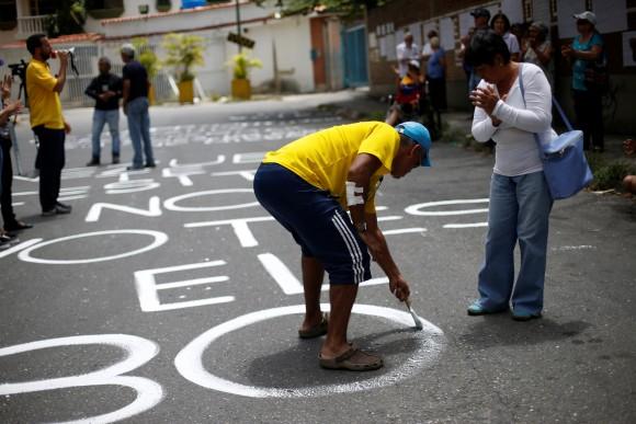 An opposition supporter paints on the road outside a school during a rally against the National Constituent Assembly, outside a school where a polling center will be established for a Constitutional Assembly election next Sunday, in Caracas, Venezuela, July 24, 2017. (Reuters/Andres Martinez Casares)