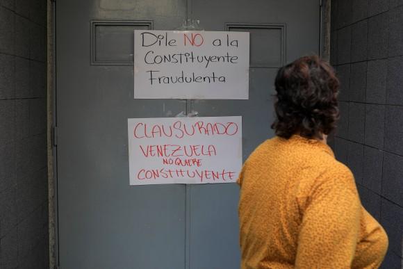 A woman walks past placards that read "Say no to the fraudulent constituent" (top) and "Closed. Venezuela does not want constituent" at the door of a school where the polling center will be established for a Constitutional Assembly election next Sunday, in Caracas, Venezuela July 24, 2017. (Reuters/Marco Bello)