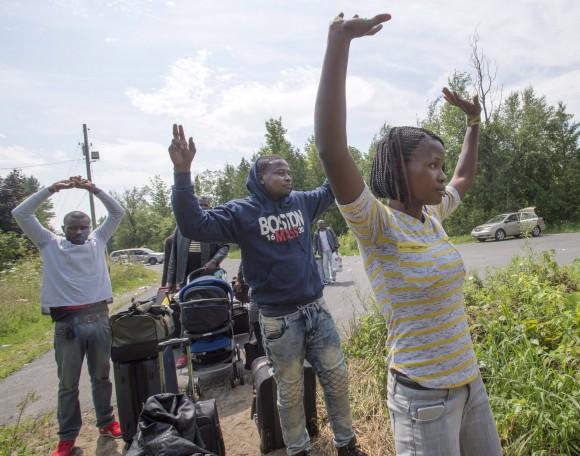 A group of asylum seekers raise their arms as they approach RCMP officers while crossing the Canadian border at Champlain, N.Y., on Aug. 4, 2017. (The Canadian Press/Ryan Remiorz)