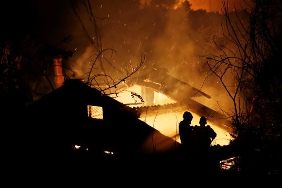 Firefighters try to extinguish a fire in a house as a wildfire burns near the village of Kalamos, north of Athens, Greece, August 13, 2017. (Reuters/Costas Baltas)
