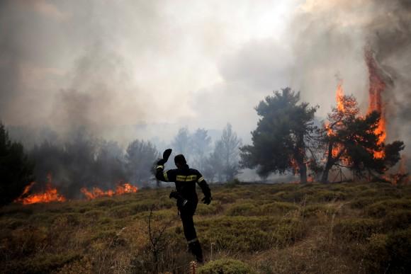 A firefighter walks on a field as flames rise during a wildfire near the village of Kapandriti, north of Athens, Greece, August 15, 2017. (Reuters/Alkis Konstantinidis)
