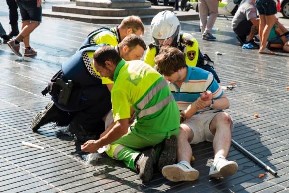 A person is helped by Spanish policemen and two men after a van ploughed into the crowd, killing at least 13 people and injuring around 100 others on the Rambla in Barcelona on Aug. 17, 2017. (Nicolas Carvalho Ochoa/AFP/Getty Images)