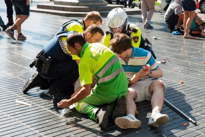 A person is helped by Spanish policemen and two men after a van ploughed into the crowd, killing at least 13 people and injuring around 100 others on the Rambla in Barcelona on August 17, 2017. (NICOLAS CARVALHO OCHOA/AFP/Getty Images)