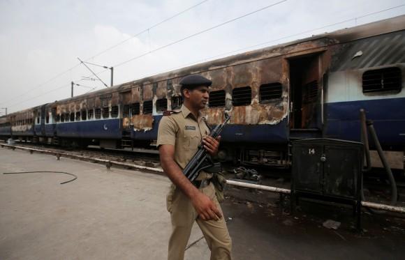 A security personnel member walks past a burnt carriage of a train near a railway station in New Delhi, India, August 26, 2017. (Reuters/Adnan Abidi)