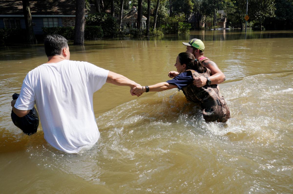Melissa Ramirez (C) struggles against the current flowing down a flooded street helped by Edward Ramirez (L) and Cody Collinsworth as she tried to return to her home for the first time since Harvey floodwaters arrived in Houston, Texas on Sept. 1, 2017. (REUTERS/Rick Wilking)