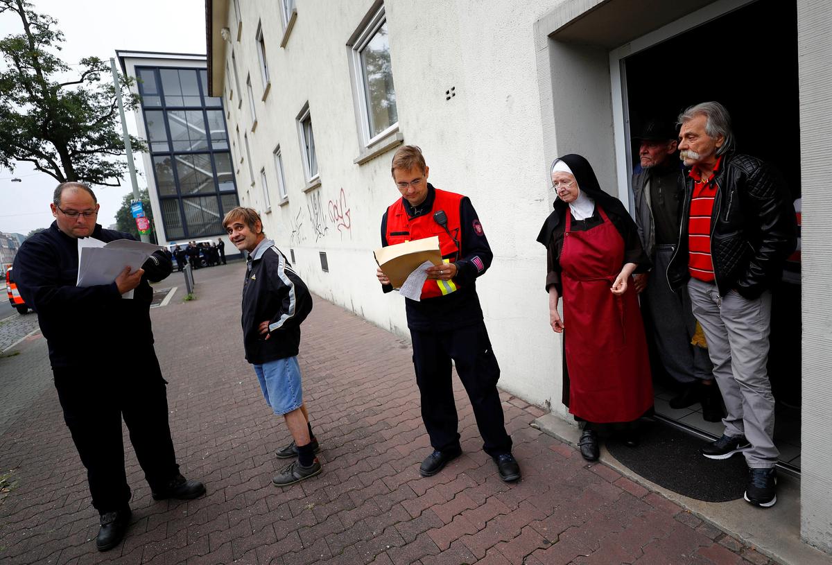 Sister Sigrid (3rdR) talks to firefighters and police officers as she observes the evacuation of her nursery home for homeless people as 60,000 people in Germany's financial capital are about to evacuate the city while experts defuse an unexploded British World War Two bomb found during renovations on the university's campus in Frankfurt, Germany, on Sept. 3, 2017. (REUTERS/Kai Pfaffenbach)