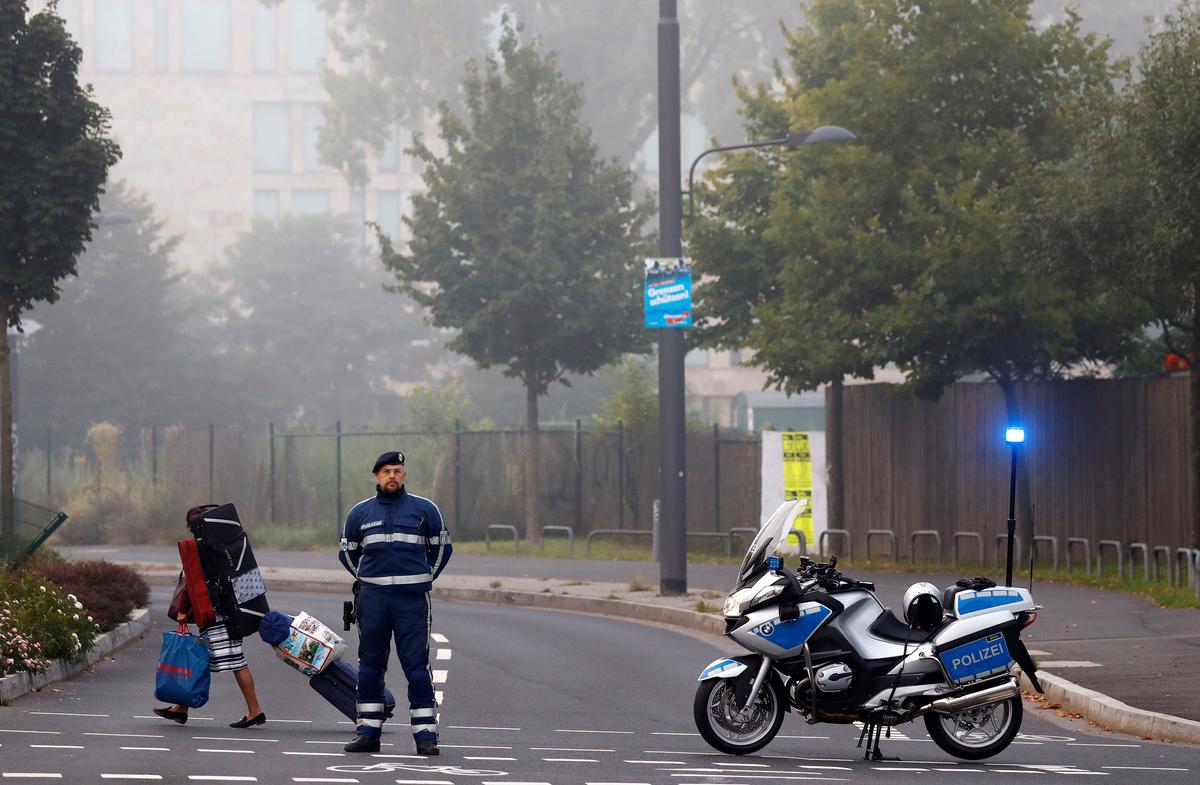 A woman carries her belongings walking past a police officer as some 60,000 people in Germany's financial capital are about to evacuate the city while experts defuse an unexploded British World War Two bomb found during renovations on the university's campus in Frankfurt, Germany on Sept. 3, 2017. (REUTERS/Kai Pfaffenbach)