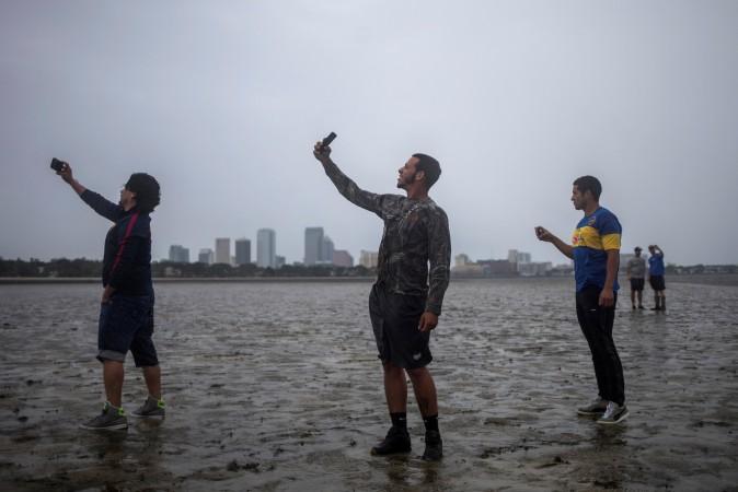 The Tampa skyline is seen in the background as local residents (L-R) Rony Ordonez, Jean Dejesus, and Henry Gallego take photographs after walking into Hillsborough Bay ahead of Hurricane Irma in Tampa, Fla., on Sept. 10, 2017. (Reuters/Adrees Latif)