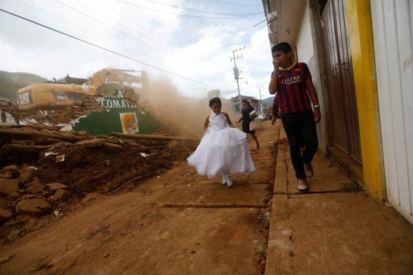 A girl in a communion dress walks past a demolition machine tearing down a house damaged by an earthquake, in Tecomatlan, Mexico, on Sept. 25, 2017 (REUTERS/Edgard Garrido)
