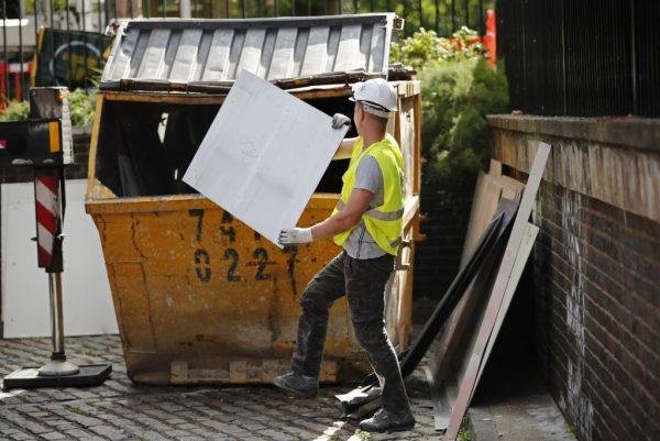 A workman throws a panel of external cladding from the facade of Braithwaite House into a skip in London, on July 3, 2017, in the wake of the Grenfell Tower fire. (Tolga Akmen/AFP/Getty Images)