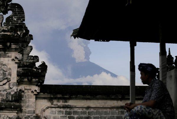 A Balinese man sits as Mount Agung volcano erupts at Lempuyang Temple in Karangasem, Bali, Indonesia November 27, 2017. (Reuters/Johannes P. Christo)