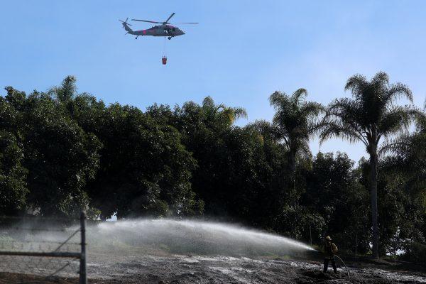 A U.S. military helicopter from Camp Pendleton makes a water drop as a firefighter puts out a hotspot at an avocado farm after the Lilac Fire, a fast moving wildfire in Bonsall, California, U.S., December 8, 2017. (Reuters/Mike Blake)