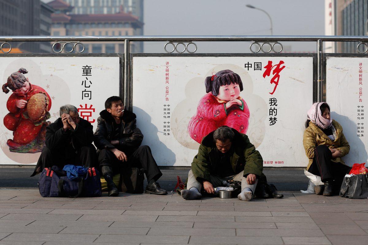 A beggar sits in front of a government propaganda at a railway station in Beijing on March 2, 2014. Developed economies are based on a broad middle class—precisely what has not been attained in China. (Lintao Zhang/Getty Images)