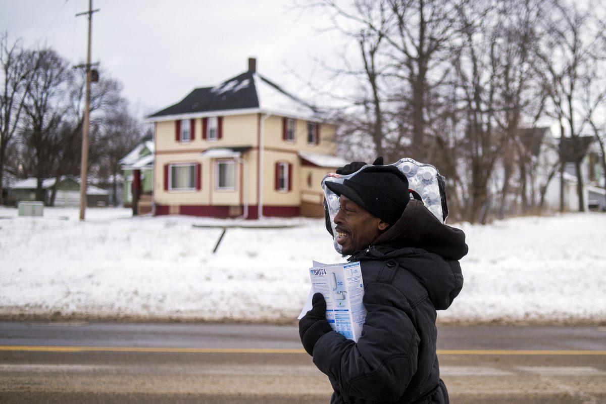 Charles Chatmon carries a free water filter and case of water away from a fire station where members of the Michigan National Guard helped distribute supplies to aid in the city's water crisis in Flint, Mich., on Jan. 13, 2016. (Jake May/The Flint Journal-MLive.com via AP)