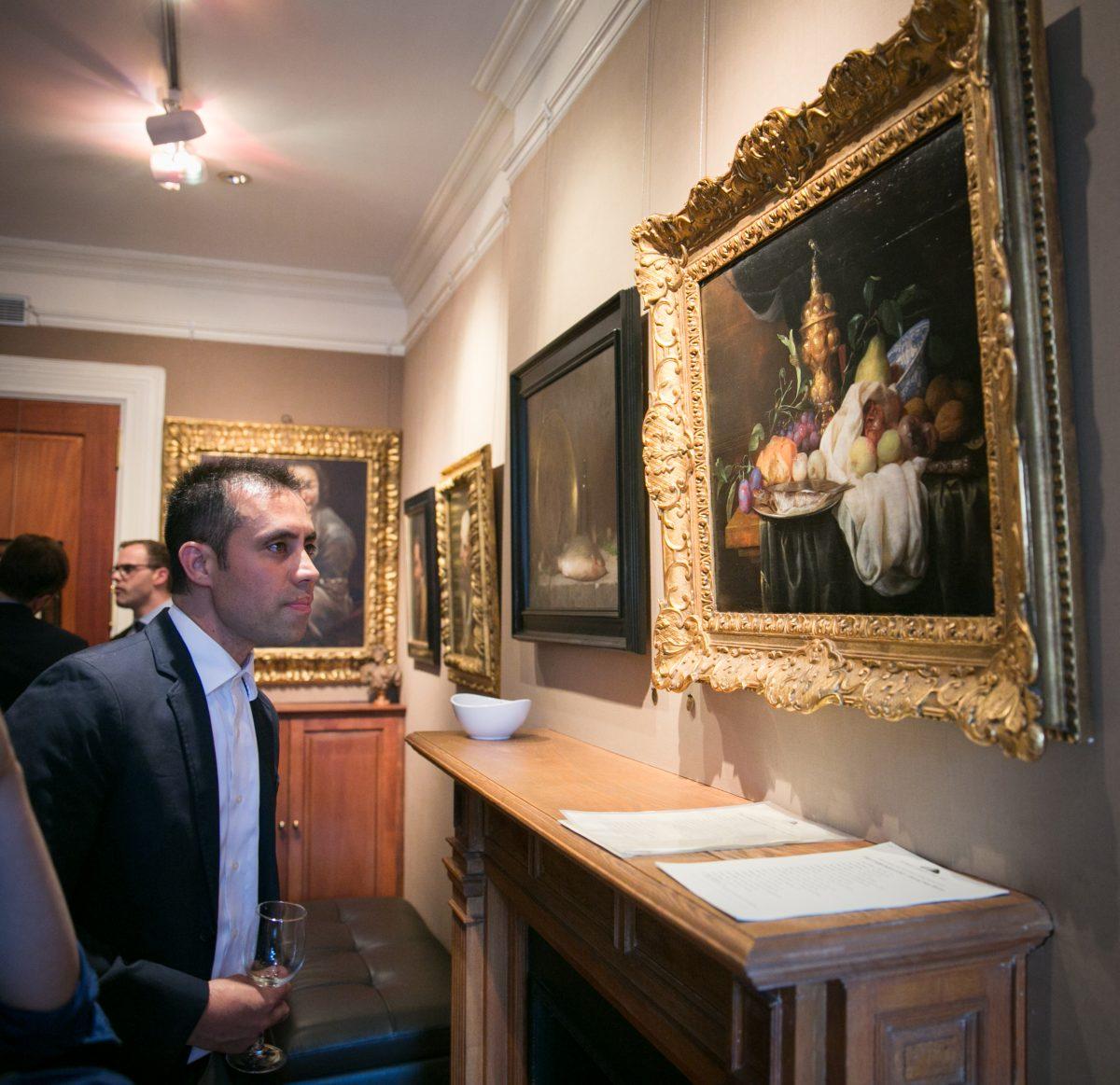 Artist and co-curator of the exhibition, Anthony Baus looks at a still life by Joris van Son (b. 1623), which hangs next to "Sea Bass" by Justin Wood (b. 1982), at the opening of "The Unbroken Line" in the Robert Simon Fine Art gallery on May 10, 2018. (Milene Fernandez/The Epoch Times)
