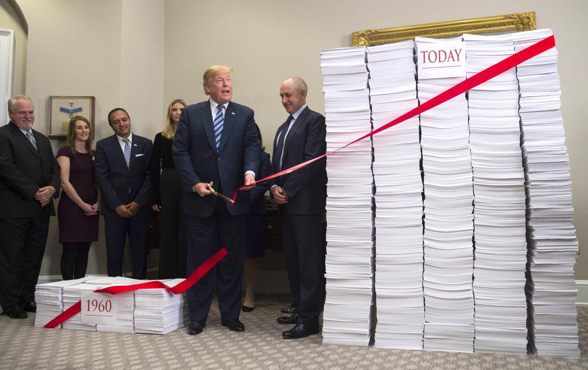 President Donald Trump uses gold scissors to cut a red tape tied between two stacks of papers representing the government regulations of the 1960s (L) and the regulations of today (R) in the Roosevelt Room of the White House on Dec. 14, 2017. (SAUL LOEB/AFP/Getty Images)
