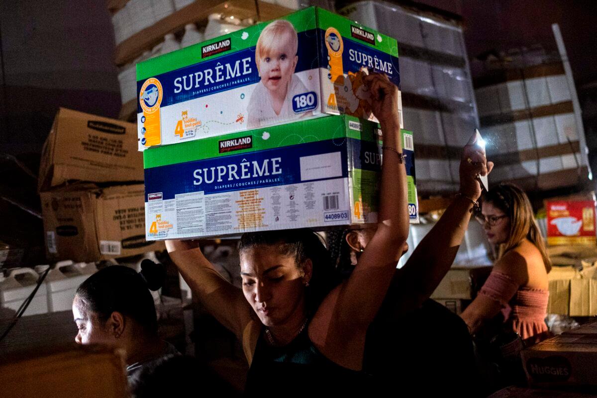 A woman carries boxes of baby diapers from warehouse filled with supplies, including thousands of cases of water, believed to have been from when Hurricane Maria struck the island in 2017 in Ponce, Puerto Rico, on Jan. 18, 2020. (Ricardo Arduengo/AFP via Getty Images)