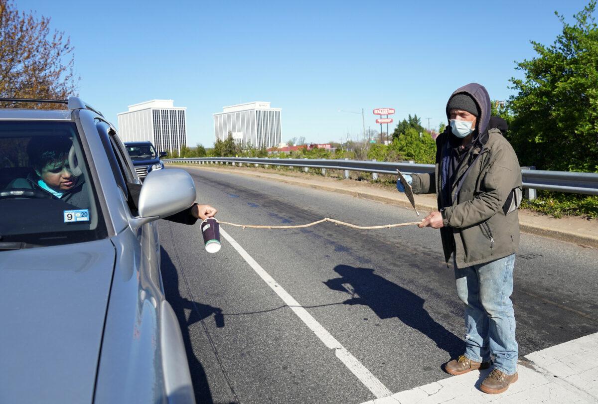 Wearing a face mask and using a stick to keep his distance amid the COVID-19 outbreak, a jobless man named Paul panhandles at an intersection in Falls Church, Virginia, on April 3, 2020. (REUTERS/Kevin Lamarque)